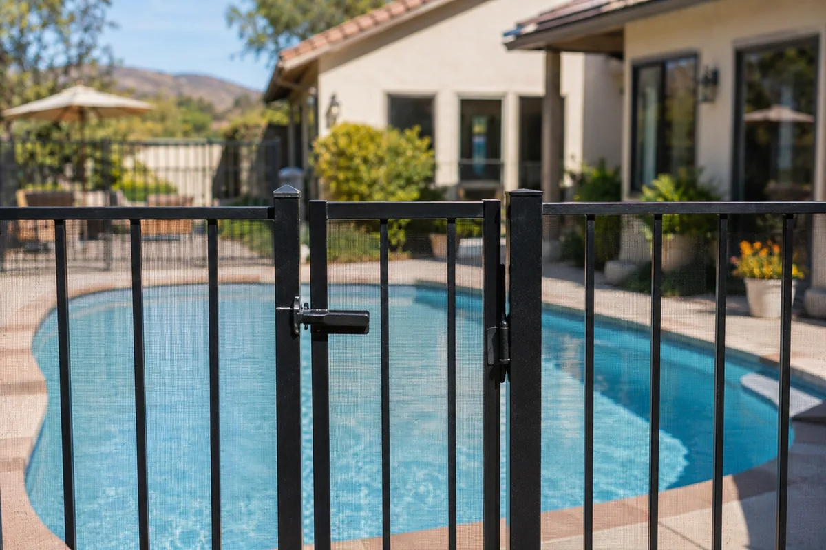 A residential pool enclosed by a metal safety fence with a self-latching gate, one of the seven drowning-prevention features SB 442 requires an inspection report to document