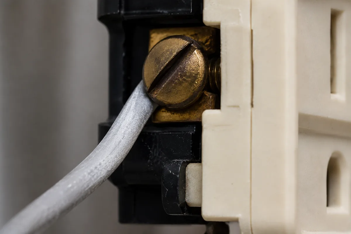 Macro view of a standard receptacle removed from a wall box showing a single-strand aluminum branch wire under the screw terminal with dull gray oxidation, a common condition in 1970s El Cajon homes