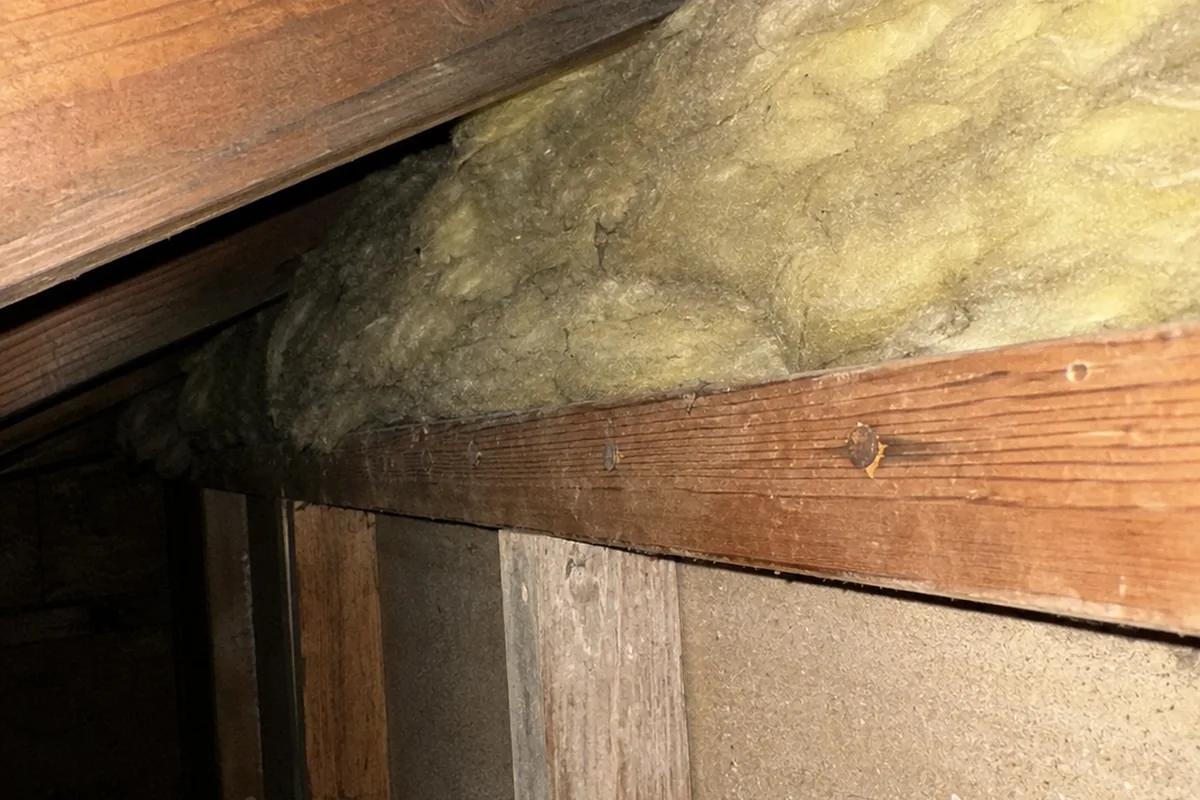 Fiberglass insulation stuffed into an attic eave completely blocking the soffit vent opening behind it
