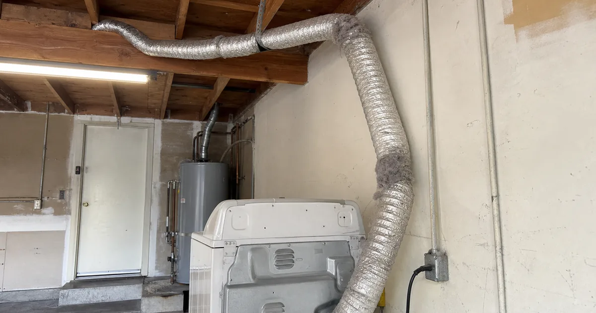 A dryer exhaust vent cap on the side of a Bellflower home with visible lint buildup around the louvers