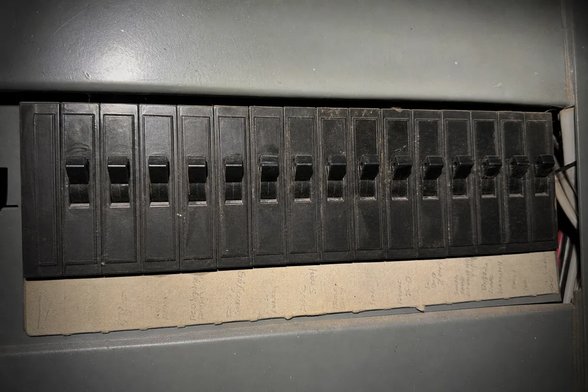 A tight row of plain black toggle breakers in a panel with no AFCI or GFCI test buttons on any of them