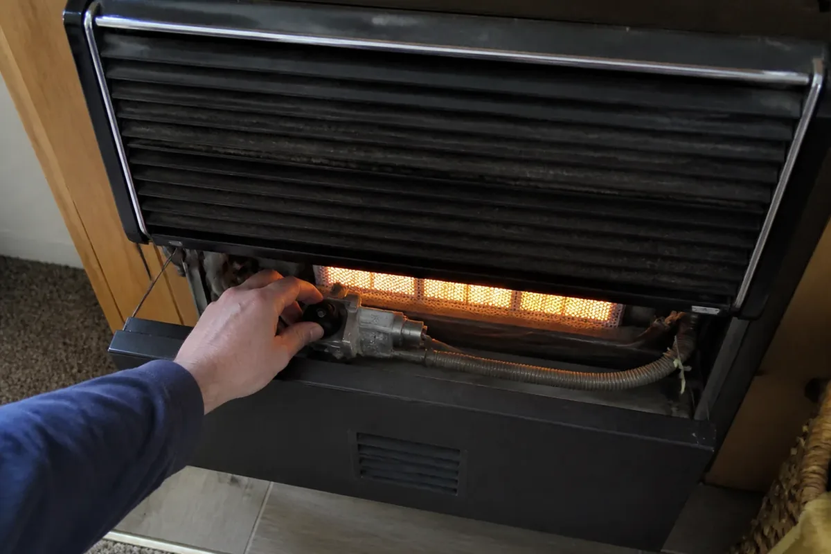 A hand checking an unvented heater’s control knob and pilot assembly for visible wear during an inspection