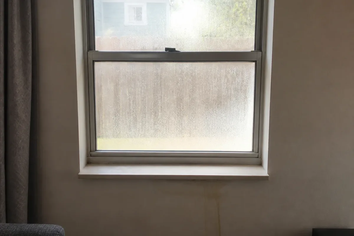 Window condensation and light staining on a wall near an unvented gas heater in a converted room, shown in ambient interior daylight
