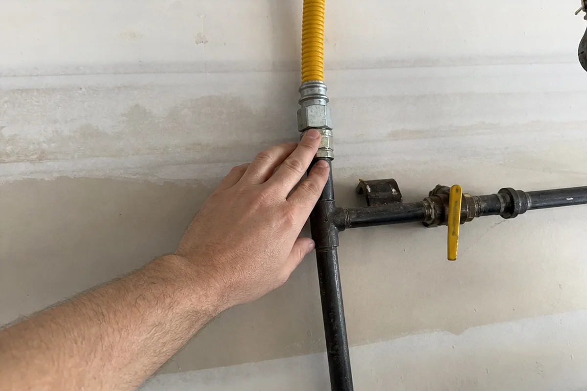 Hand tracing a run of yellow CSST tubing down to a bare black-iron manifold with no bonding clamp visible, a gas shutoff valve nearby