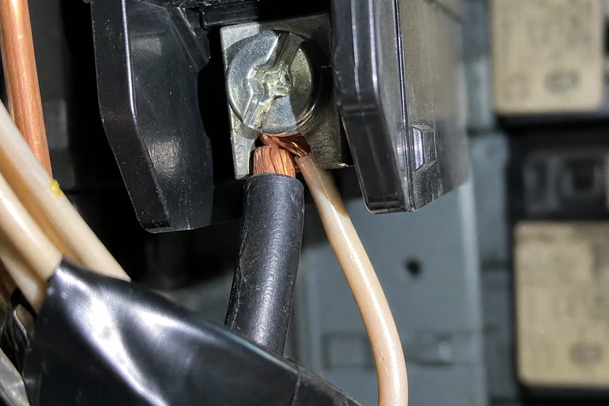 A close macro view of a breaker terminal with two black insulated conductors pinched under a single screw lug, one wire visibly less seated than the other