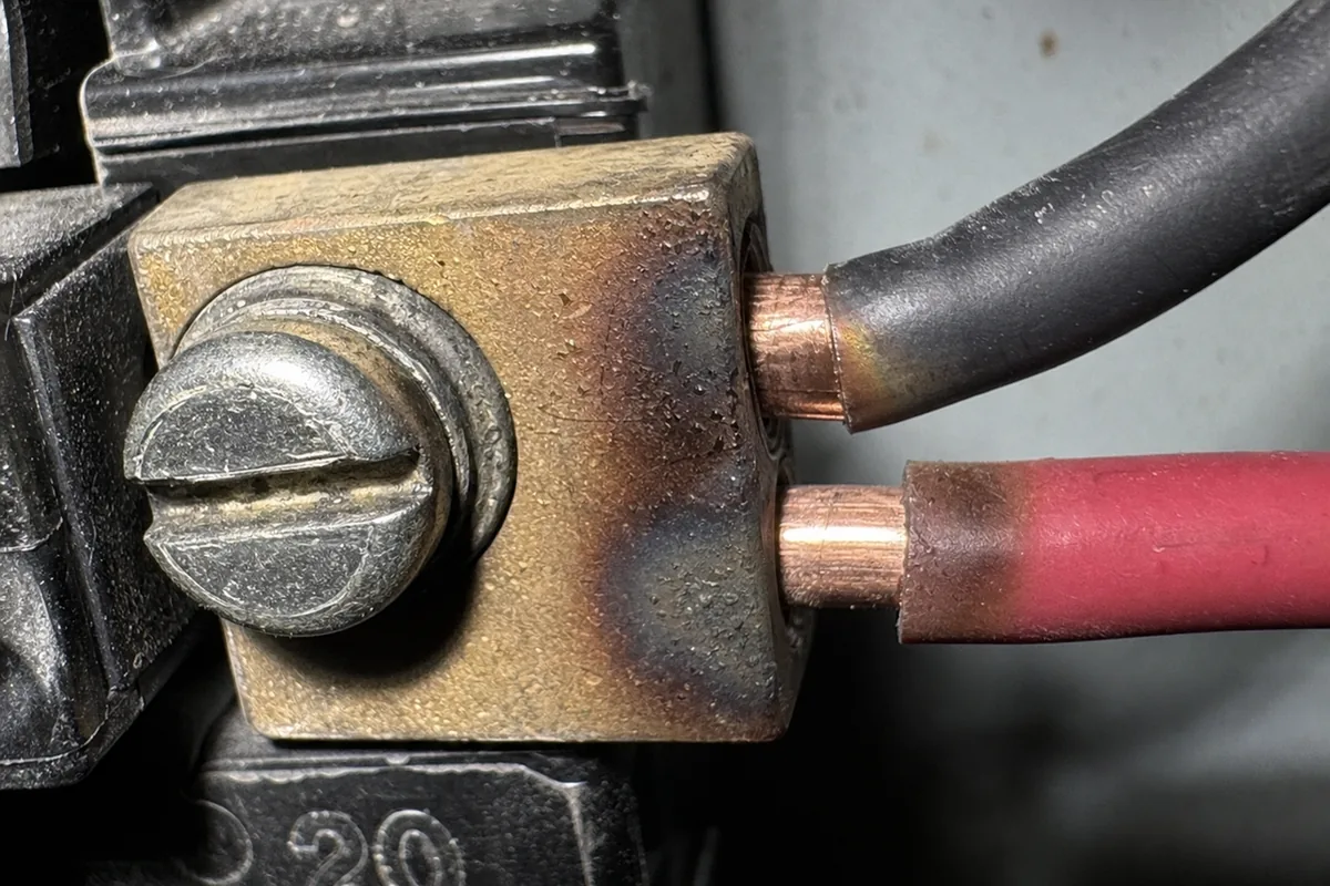 Extreme close-up of a double-tapped breaker lug showing heat discoloration and browning on the brass terminal where a loose connection has generated arc heat
