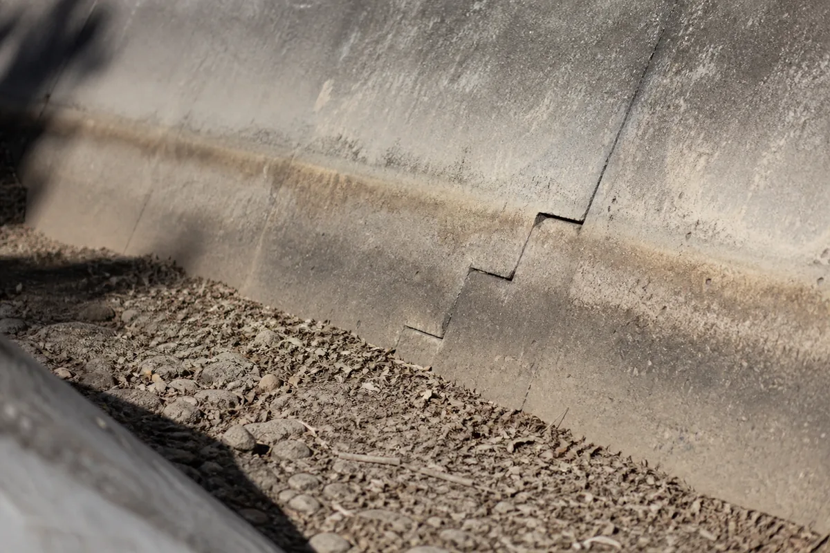 Macro view of a concrete V-ditch drainage channel half-filled with dried silt, rock, and leaf debris with a stair-step crack