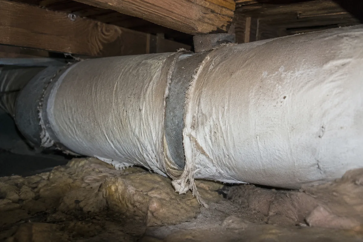 Old whitish cloth-like asbestos-style wrap around a heating duct in an attic of a mid-century home