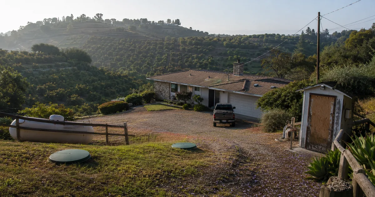 Fallbrook grove estate with septic risers, propane tank, and well pump house visible in morning haze