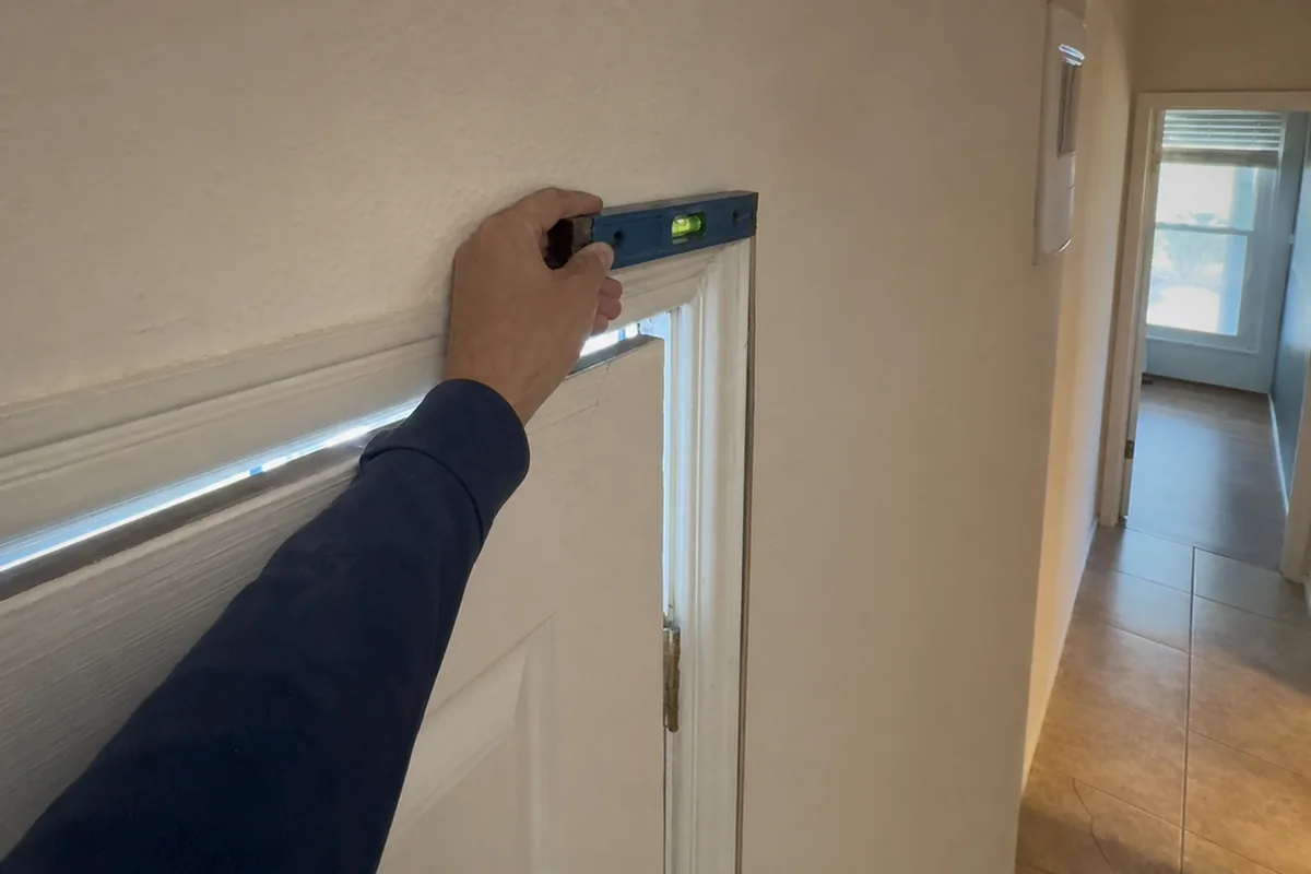 Home inspector's hand holding a torpedo level against a door frame with an uneven gap at the top corner