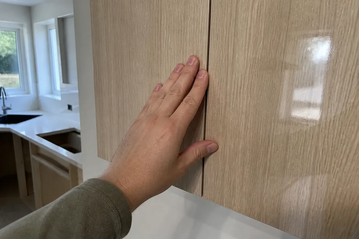 A hand checking the fit and seam of a new particleboard cabinet door during an inspection walkthrough