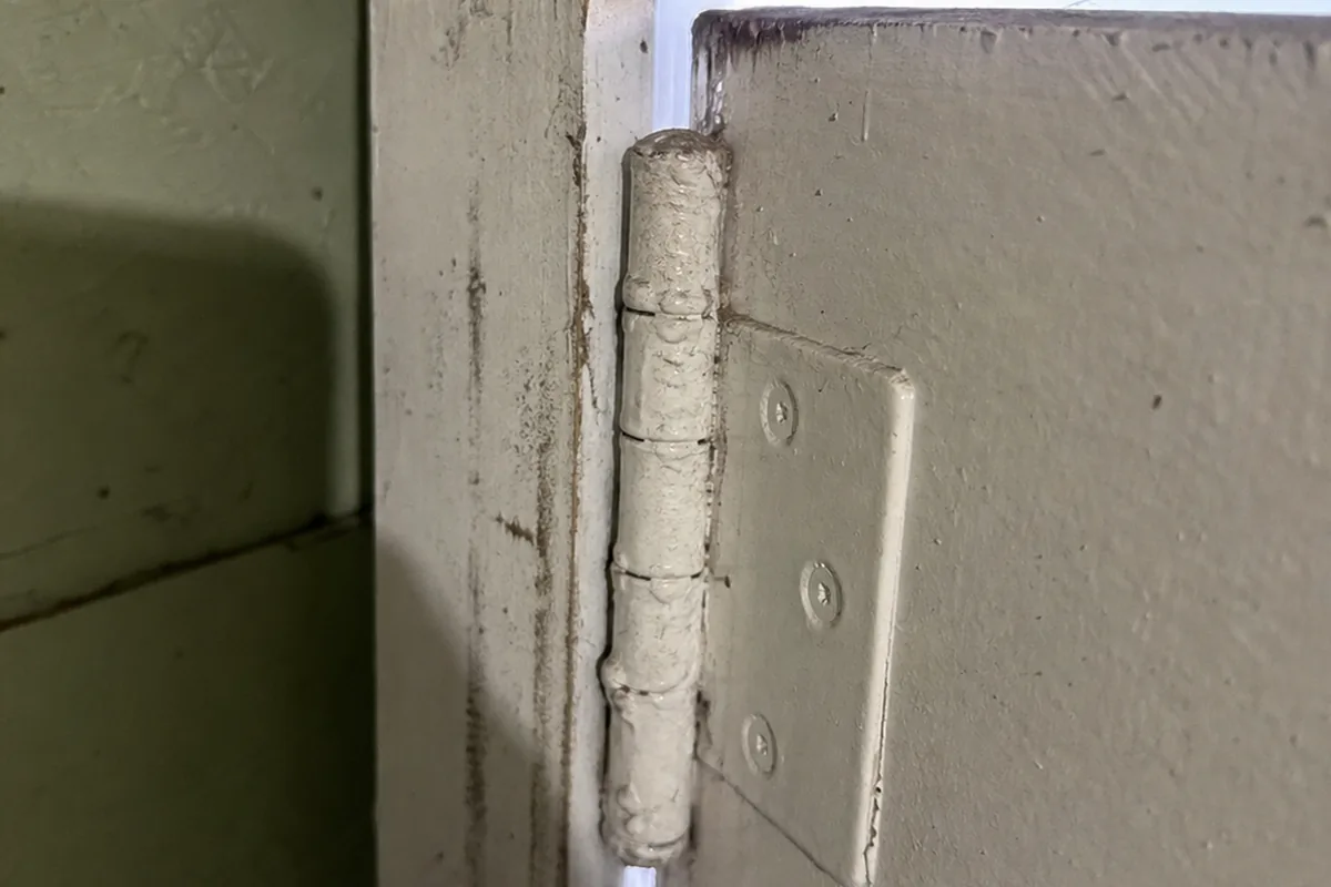 Close macro of a plain painted butt hinge on a garage-to-house door with no spring-loaded self-closing mechanism or overhead closer arm present