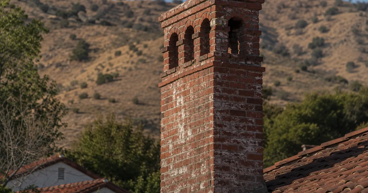 Home inspector examining a tall unreinforced brick chimney on an older Glendale home below the foothills