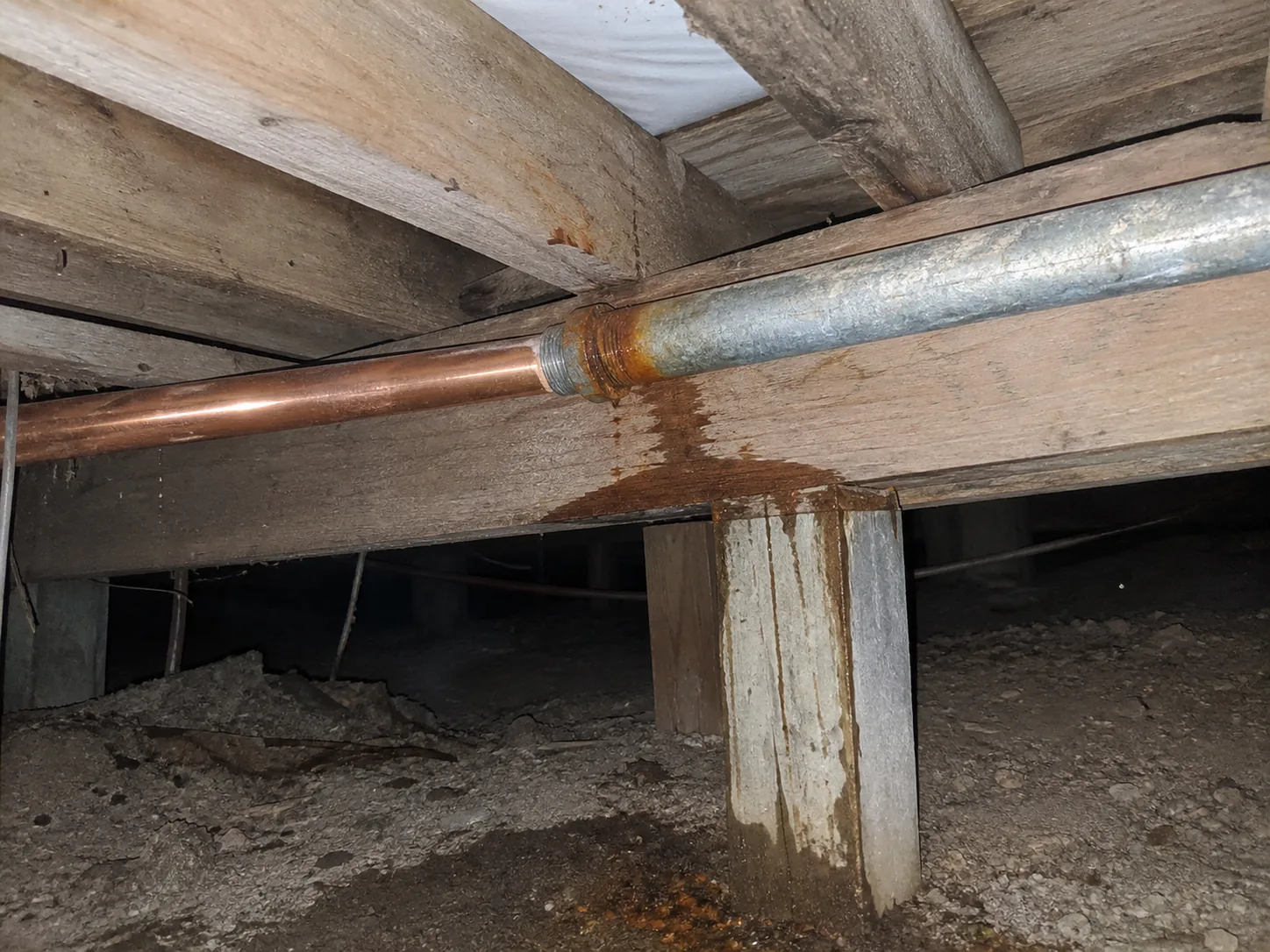 A copper water line joined directly to an older galvanized steel pipe at a threaded transition fitting under a Hermosa Beach home, with rust colored staining spreading from the joint