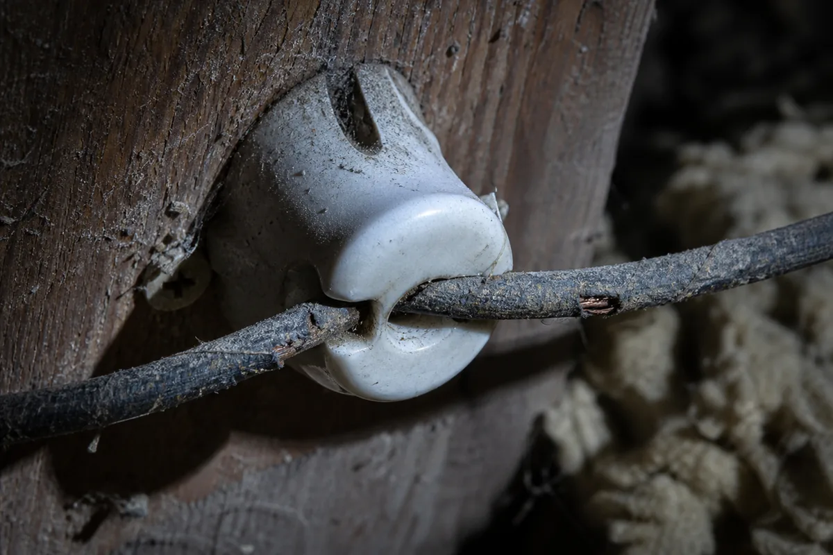 Macro view of a white ceramic knob on an attic joist holding an old conductor with cracked, frayed cloth insulation