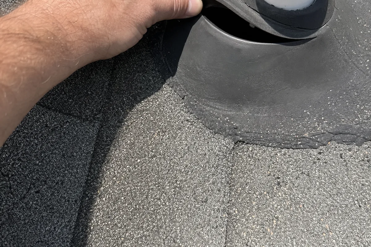 Hand lifting the split rubber collar of a roof vent boot away from the pipe, straight-down angle