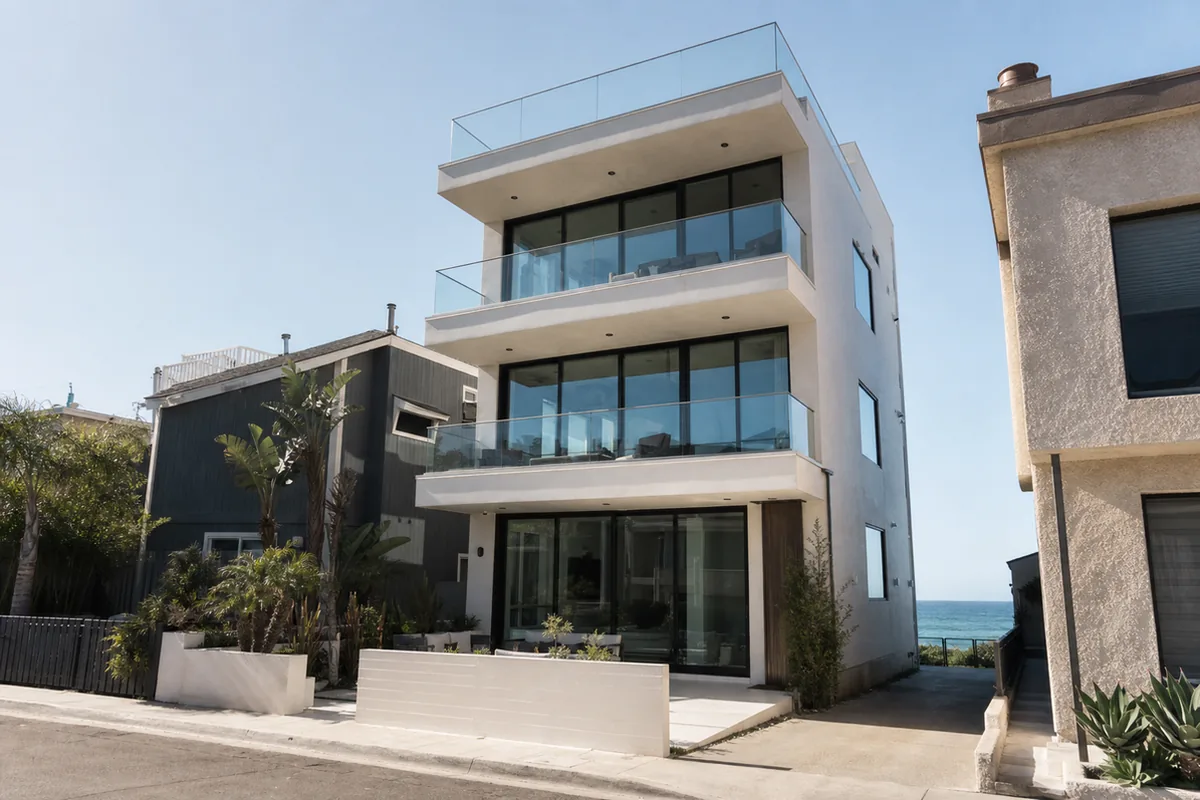 A tall modern four-level Manhattan Beach home on a narrow lot with stacked cantilevered balconies and a glass-railed roof deck facing the ocean