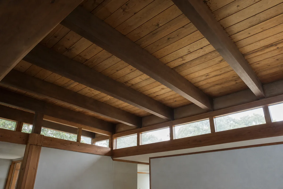 Interior view looking up at an exposed mid-century post-and-beam ceiling of dark wood beams and tongue-and-groove decking with a clerestory window band