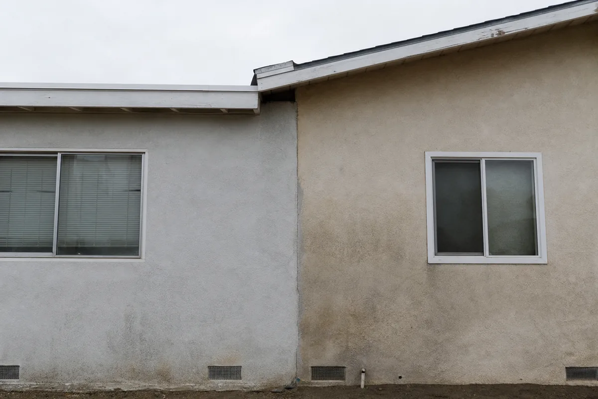 Exterior seam where a room addition meets an original postwar house, two different rooflines and two slightly different shades of stucco meeting at a visible vertical joint