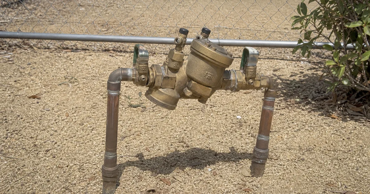 A brass double-check backflow prevention assembly mounted on a copper irrigation supply line at a Moreno Valley property, with test cocks and shutoff valves visible