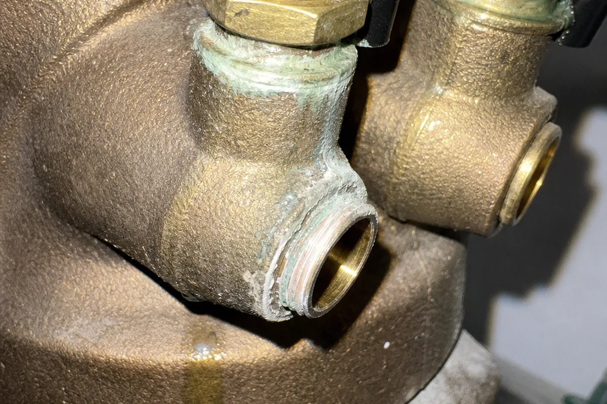 A close macro view of corroded brass test cocks on a backflow prevention assembly, with mineral staining and a missing protective cap