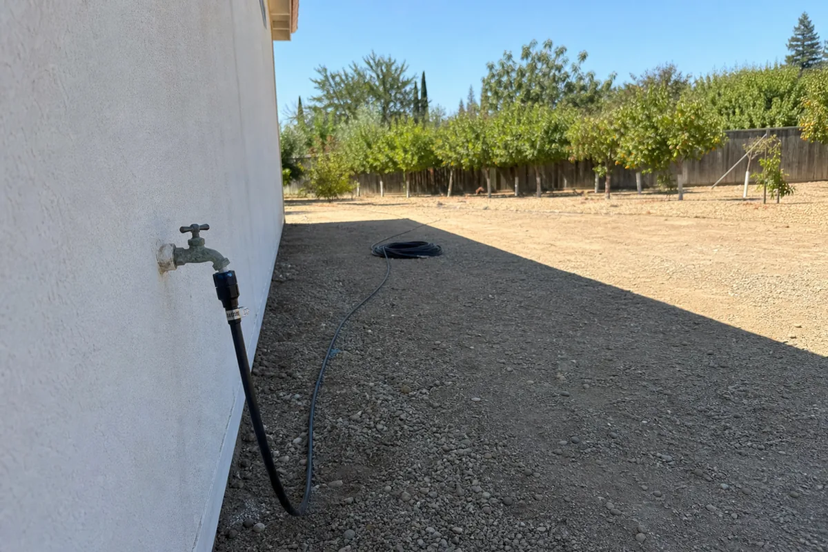 A wide exterior view of a Moreno Valley property showing a drip irrigation main line entering from a side yard hose bib with no visible backflow device attached