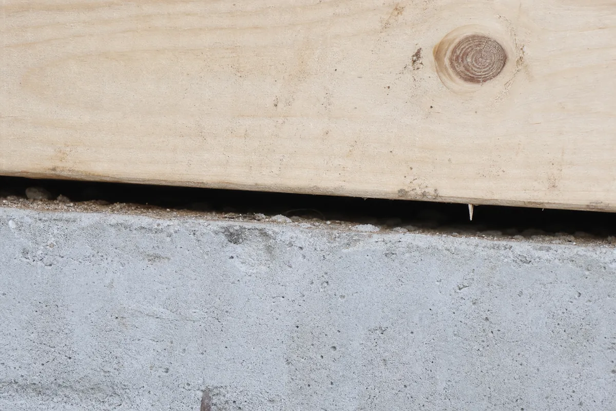 Close view inside a crawlspace of a wood mudsill resting on a concrete foundation with no anchor bolts connecting them