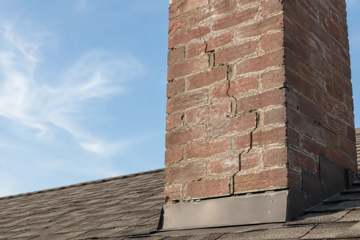 Roof-level view of a masonry chimney with a vertical stair-step mortar crack and separation at the flashing