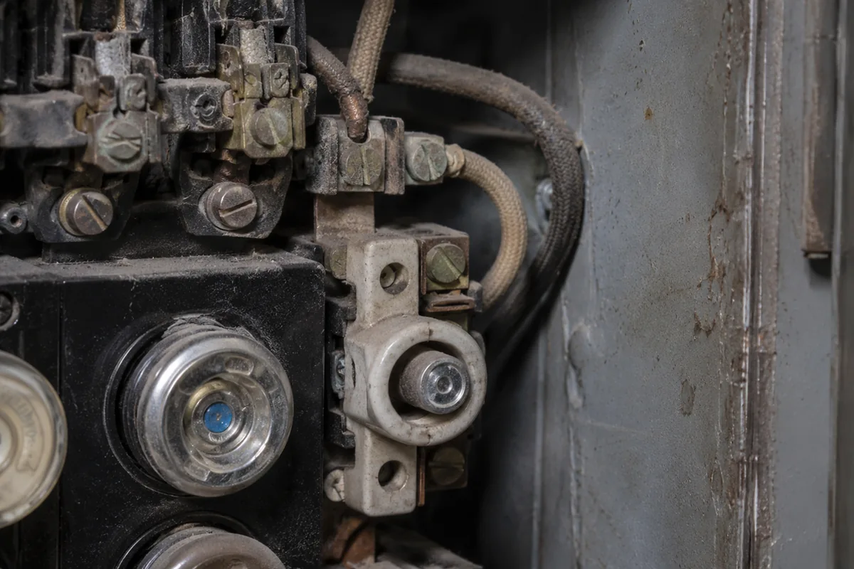 Extreme close-up of an antique residential fuse panel interior with round screw-in fuses, a ceramic pull-out block, and aged fabric-wrapped wiring