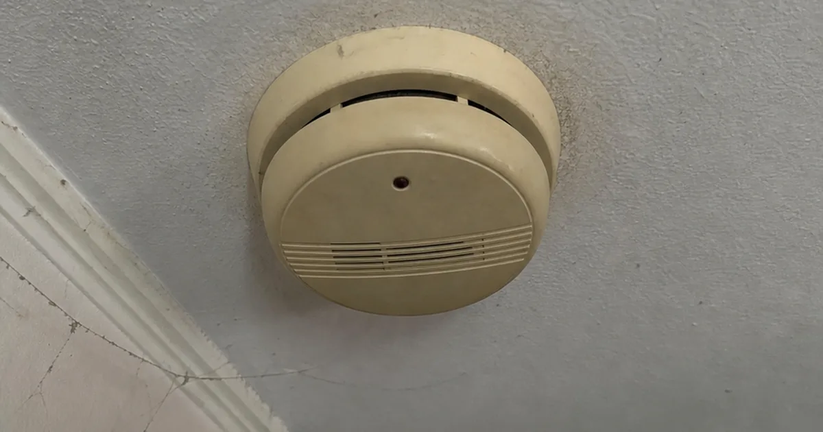 An aged, yellowed smoke alarm mounted on an Ontario hallway ceiling with a long-past manufacture date