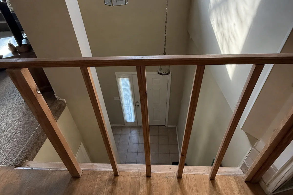 High angle looking down over an open loft landing edge with a low, wide-spaced guardrail above a full two-story drop to the entry floor below