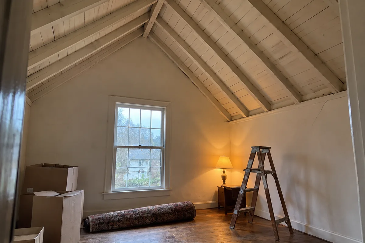 Upstairs room in an older house with the ceiling removed, exposed rafters rising to a ridge board and no horizontal board crossing the room
