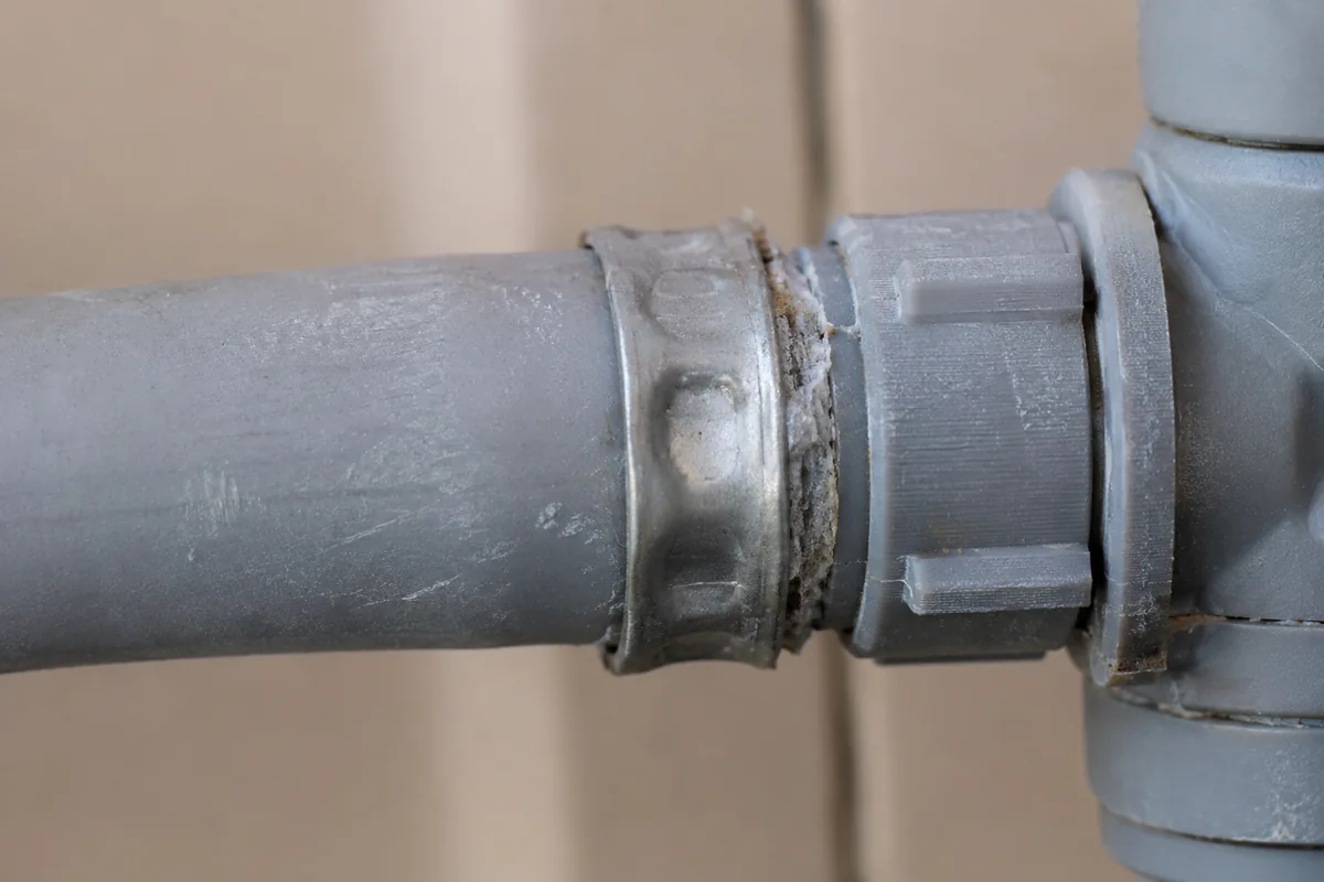 Macro view of gray polybutylene water supply pipe joined with a gray acetal plastic fitting, the connection point where the material most often fails