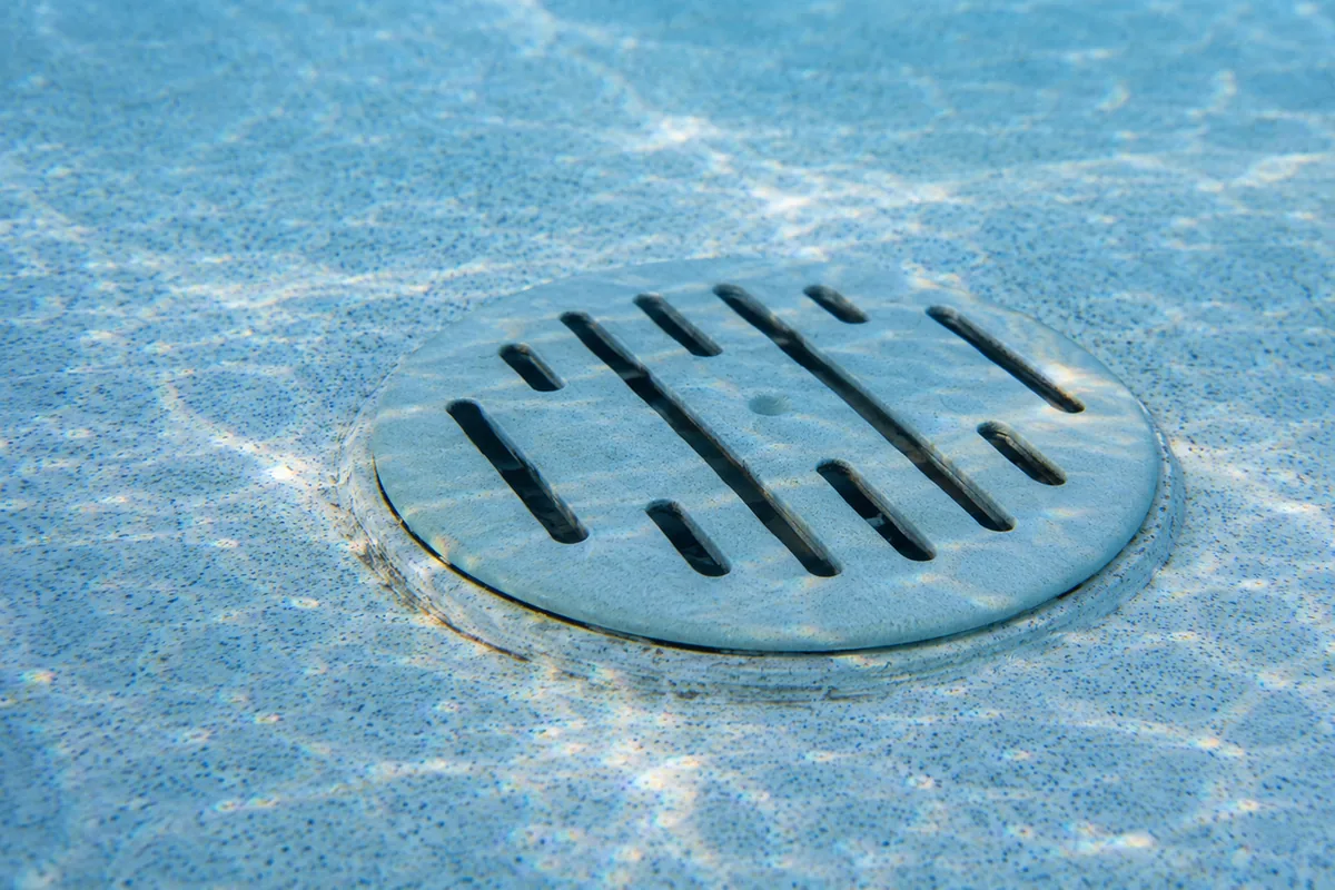 Macro view of a pool main-drain suction outlet at the bottom of a pool showing an older flat cover rather than a domed anti-entrapment cover