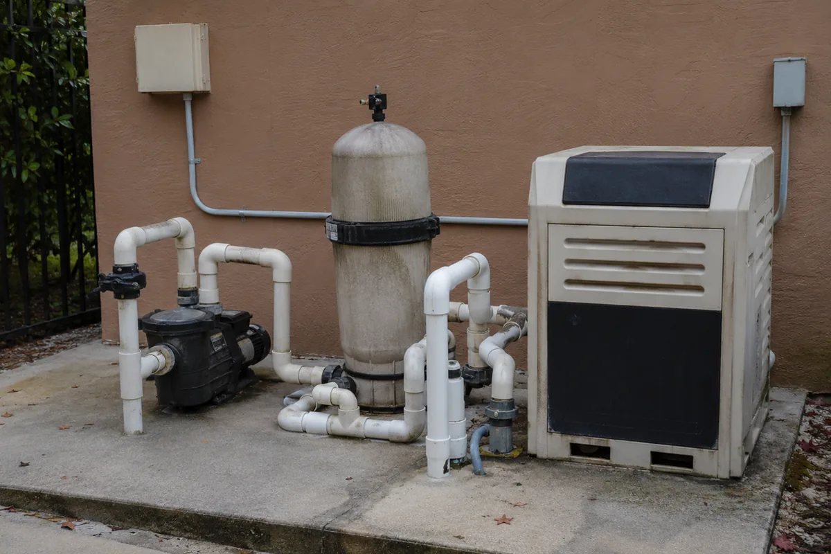 Wide view of a Beverly Hills pool equipment pad with the pump, filter, and heater installed against a stucco wall, the system an inspector evaluates