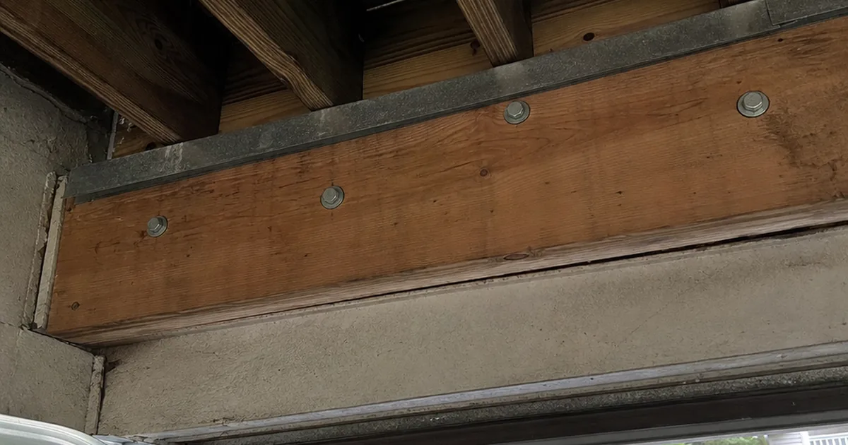 Underside view of an elevated wood deck ledger board bolted to a Redondo Beach house rim joist, showing through-bolts and flashing at the connection
