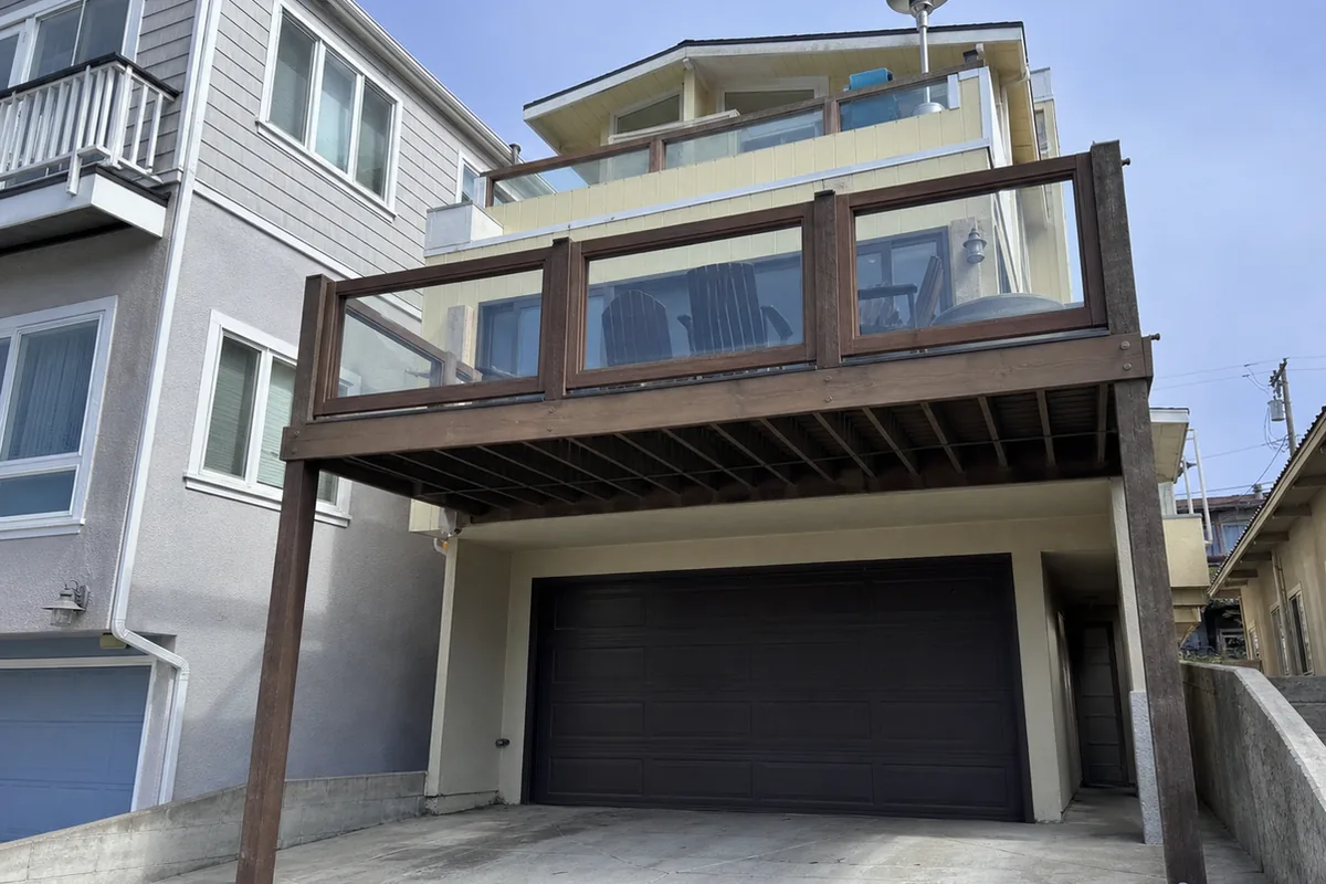 Wide exterior view of a stacked multi-level Redondo Beach home with an elevated deck cantilevered over a tuck-under garage on a narrow lot