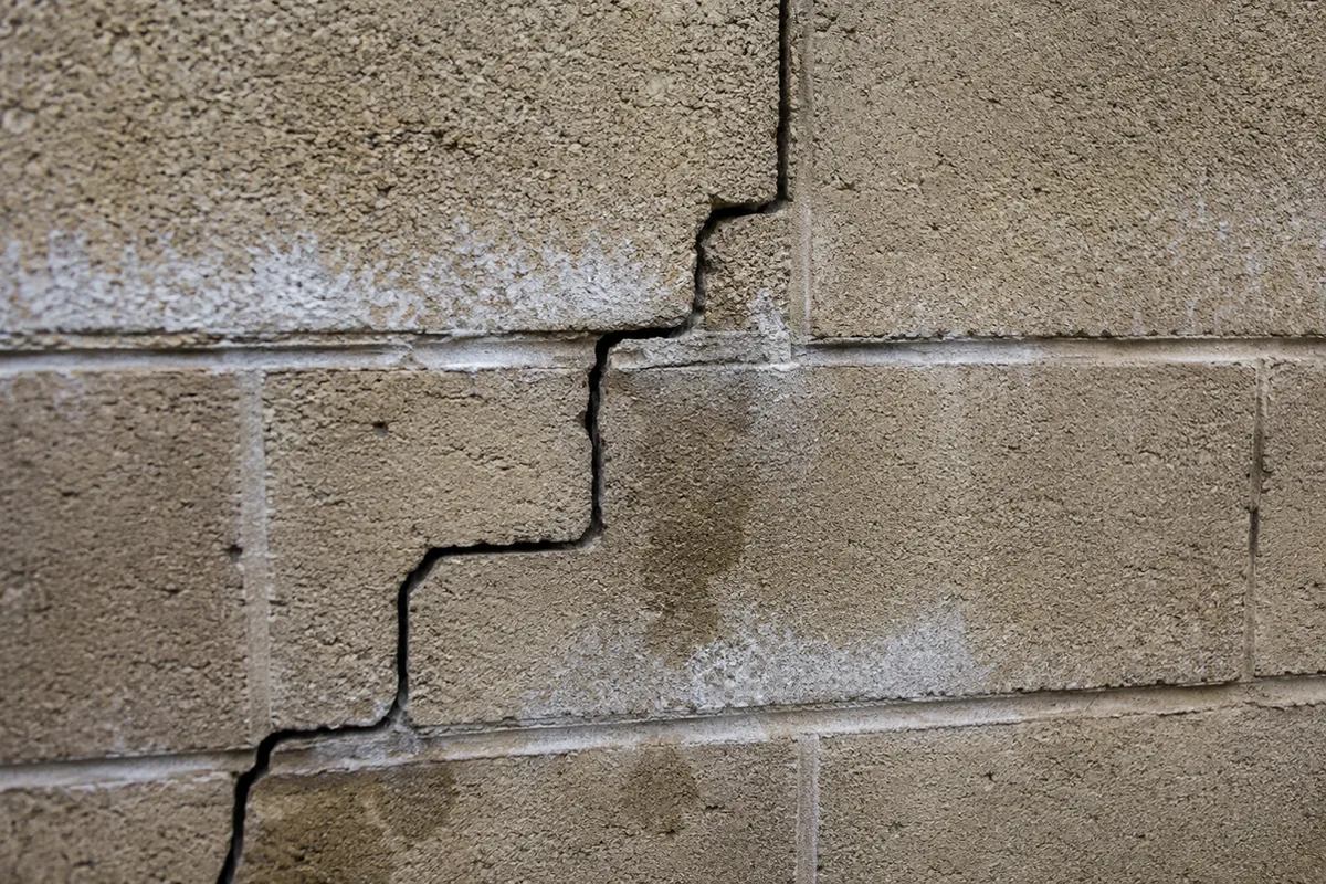 Macro view of a block retaining wall showing a stair-step crack through the courses with white efflorescence bleeding from the mortar joints