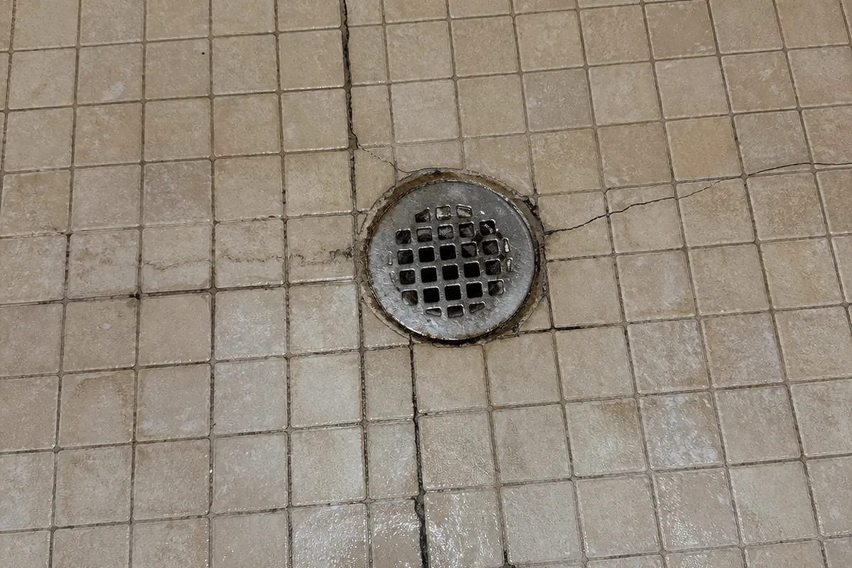Looking straight down at a tile shower floor and drain, cracked grout radiating from the drain across the pan