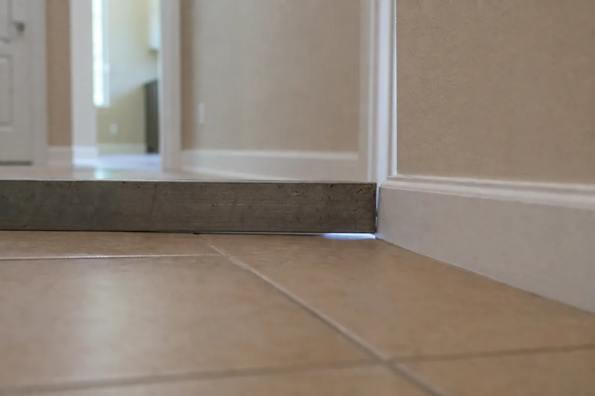 Straightedge resting across a hallway floor with a visible gap of daylight under one end where the slab dips