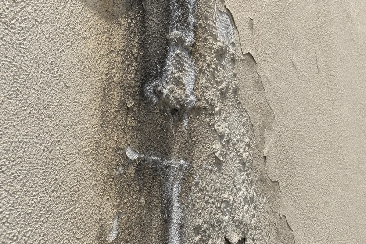 A stucco wall below a roof-to-wall junction showing a vertical brown water stain, with paint bubbling at the base and efflorescence visible on the surface