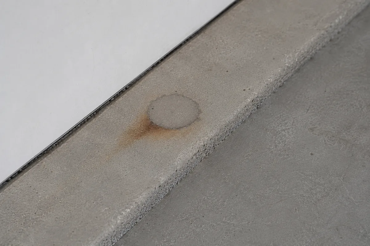 Close-up of a patched circular tendon-anchor pocket at the edge of a concrete slab, with light staining around the grout
