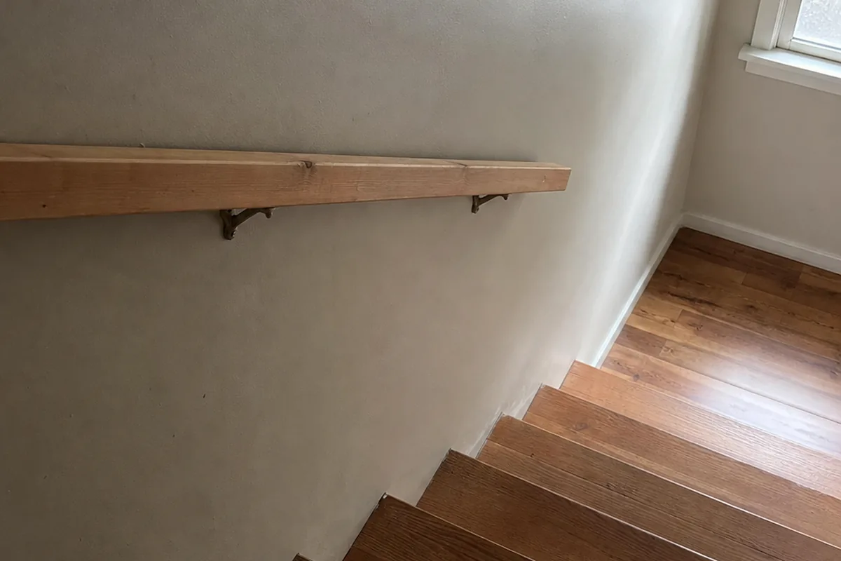 Interior staircase with a flat two-by-four handrail turned on edge that stops two steps short of the bottom, dim window light