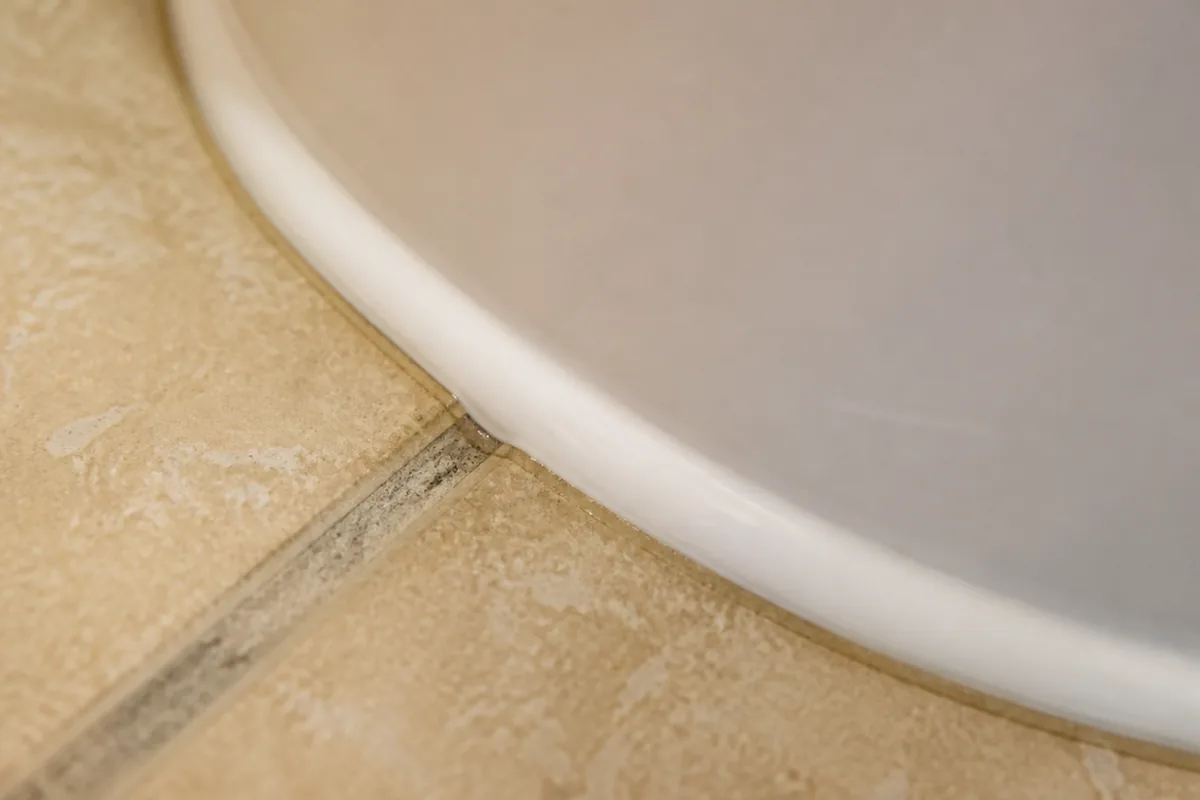 Close macro view of a caulk bead running fully around a toilet base with no gap left at the back, a subtle sign a leak may be hidden rather than fixed