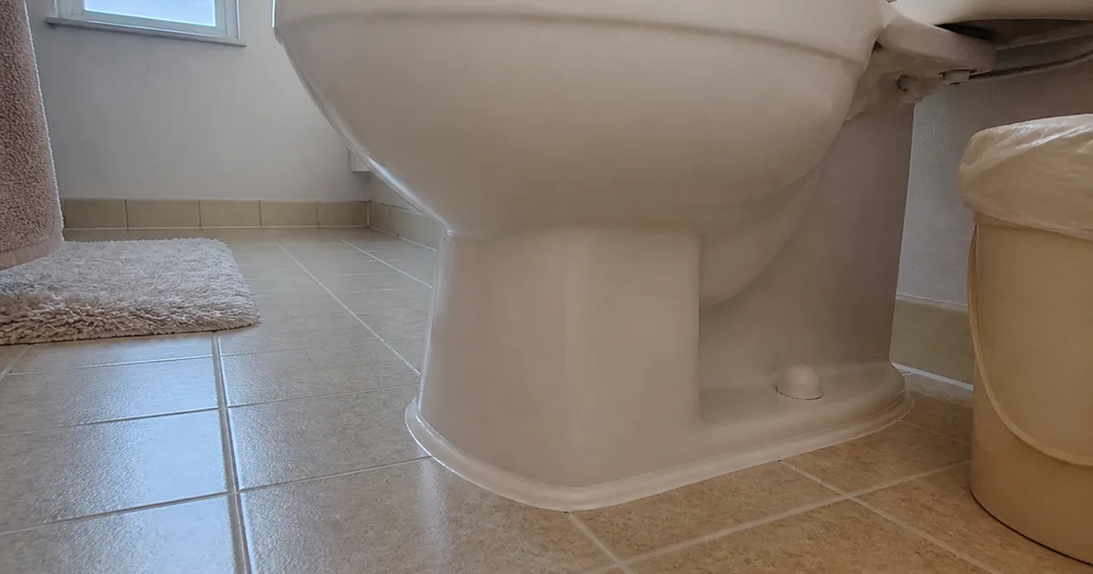 A toilet base at floor level in a Winnetka bathroom with a bead of caulk running all the way around it, hiding whether the base moves