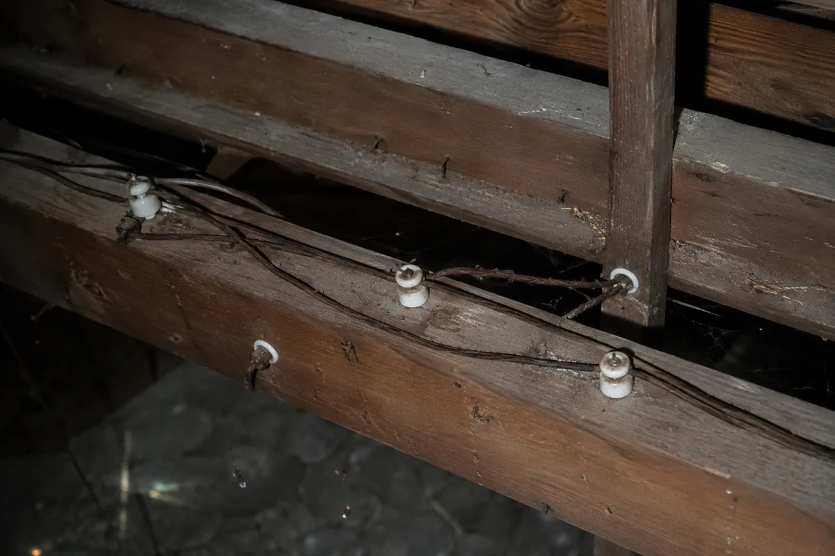 Original knob-and-tube wiring running across attic joists, with cloth-insulated conductors supported by white porcelain knobs and tubes