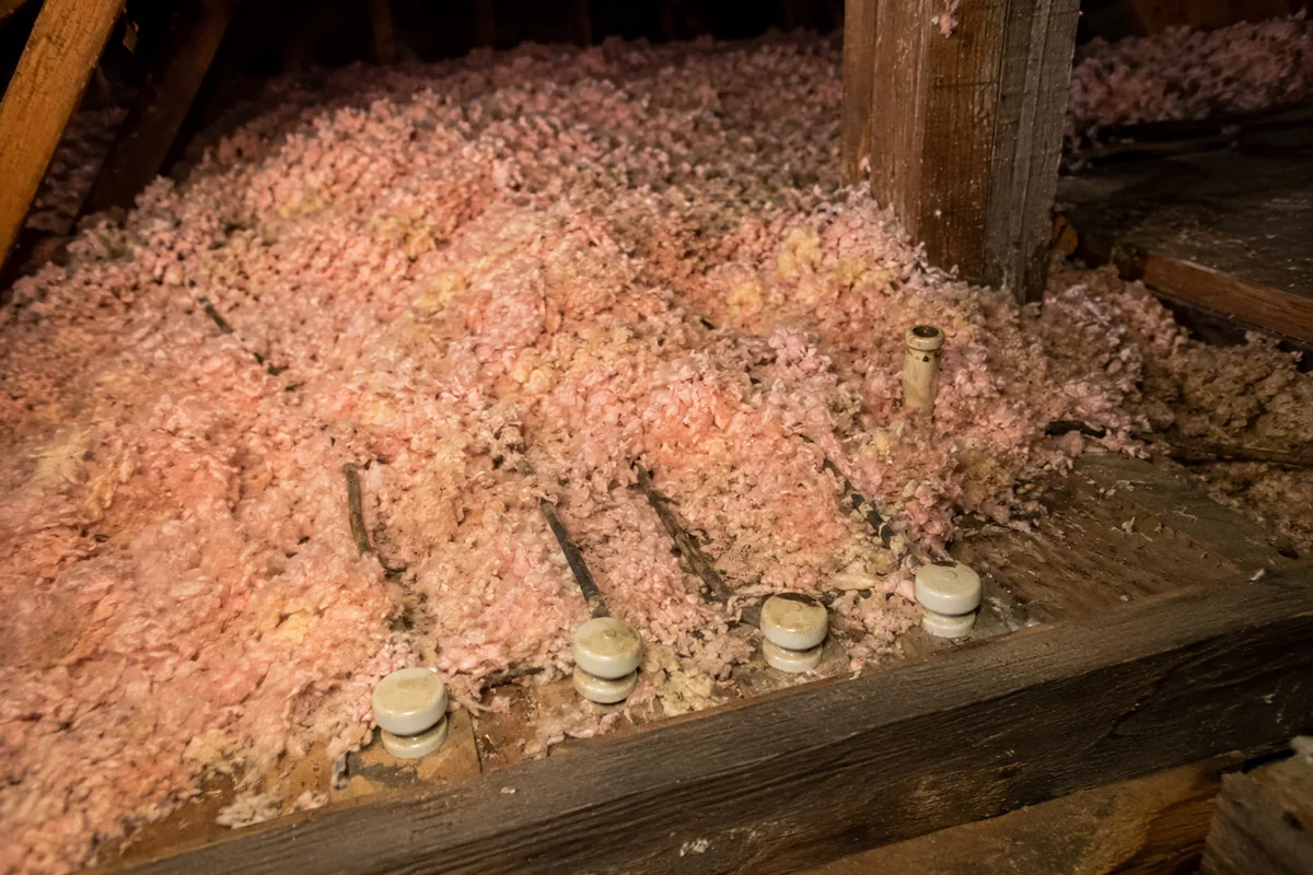 Porcelain knob-and-tube supports poking out of blown-in fiberglass insulation that has buried the original wiring, the condition that creates a fire hazard