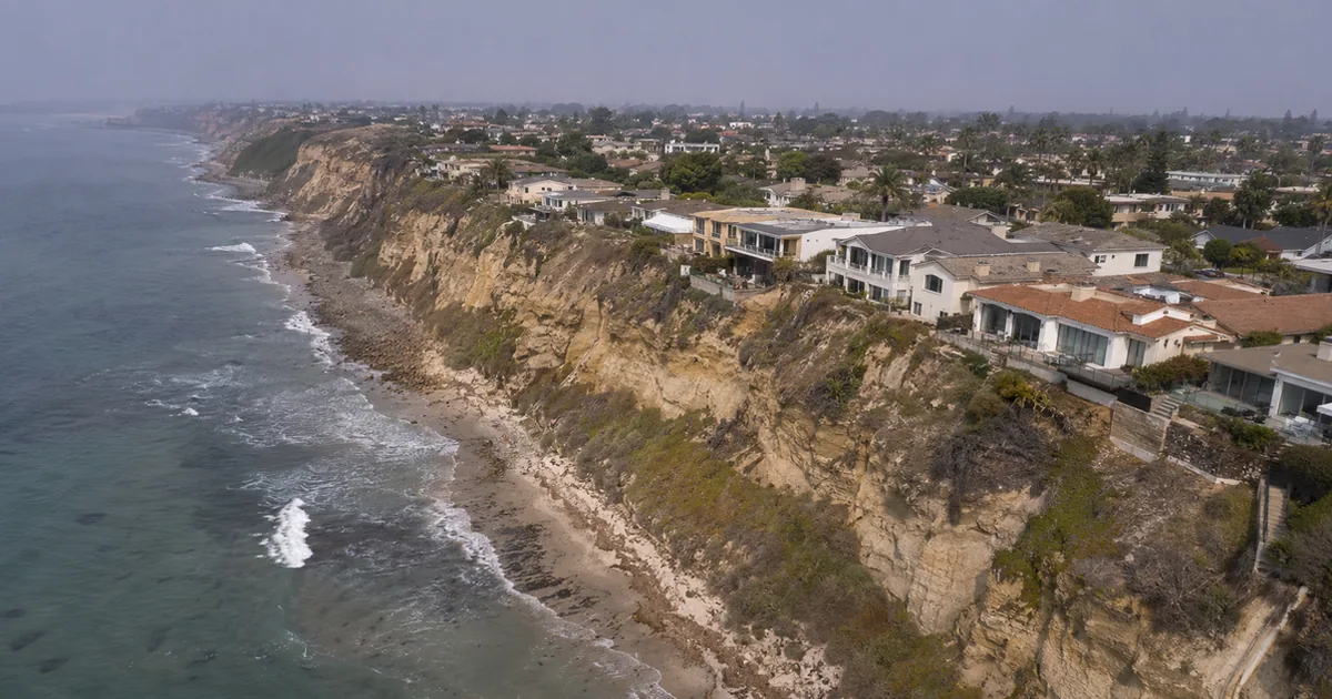 Aerial view of coastal bluff-top homes in Encinitas with eroding sandstone cliffs and Pacific Ocean waves below