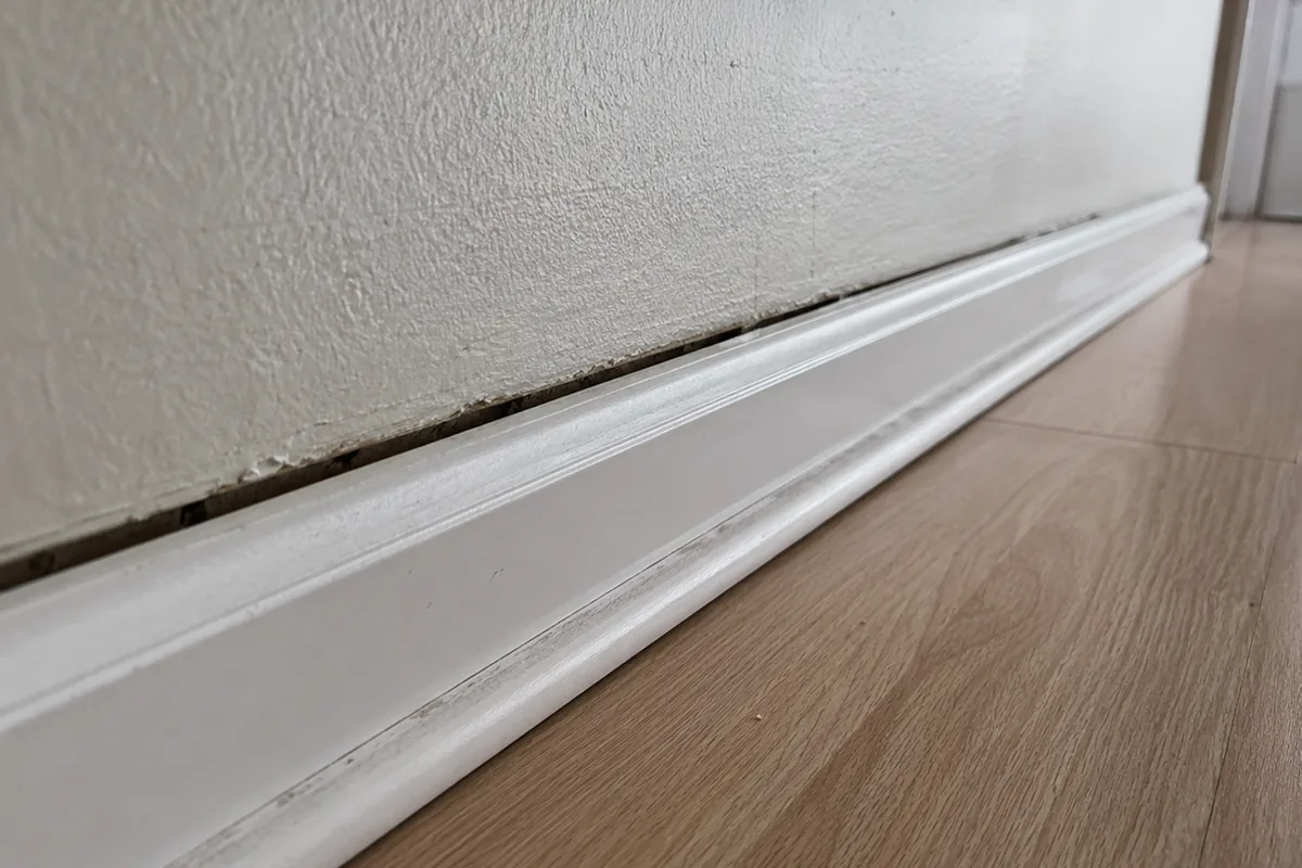 Interior baseboard separated from the wall and floor, leaving a wedge-shaped gap wider at one end
