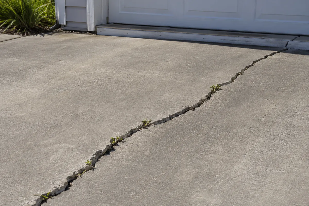 Diagonal crack across a residential concrete driveway slab continuing toward a garage door threshold